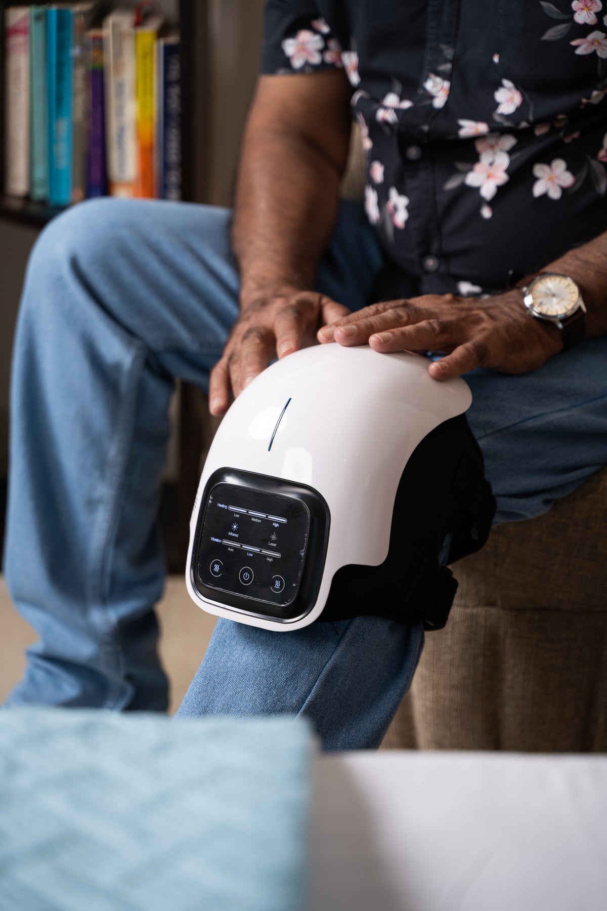 AccuFit heated knee massager with vibration function worn on the knee while sitting at home.