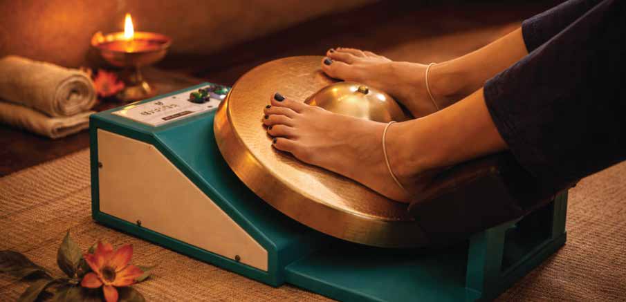Feet resting on a Kansa Thali foot massager beside a diya